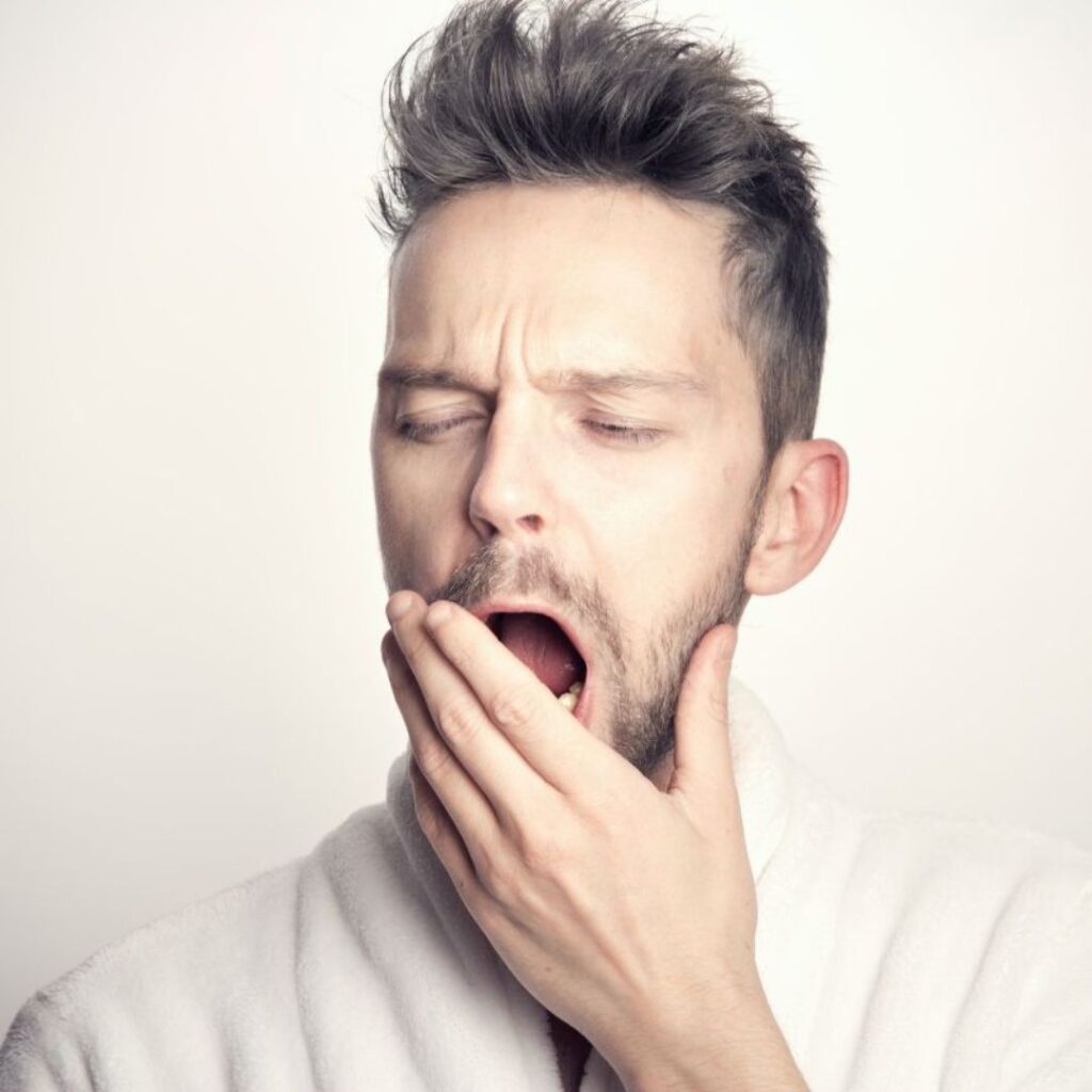 white man yawning with hand partially covering mouth